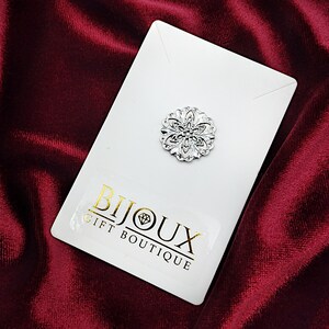 May include: A silver filigree brooch with a floral design. The brooch is on a white card with the text "Bijoux Gift Boutique".