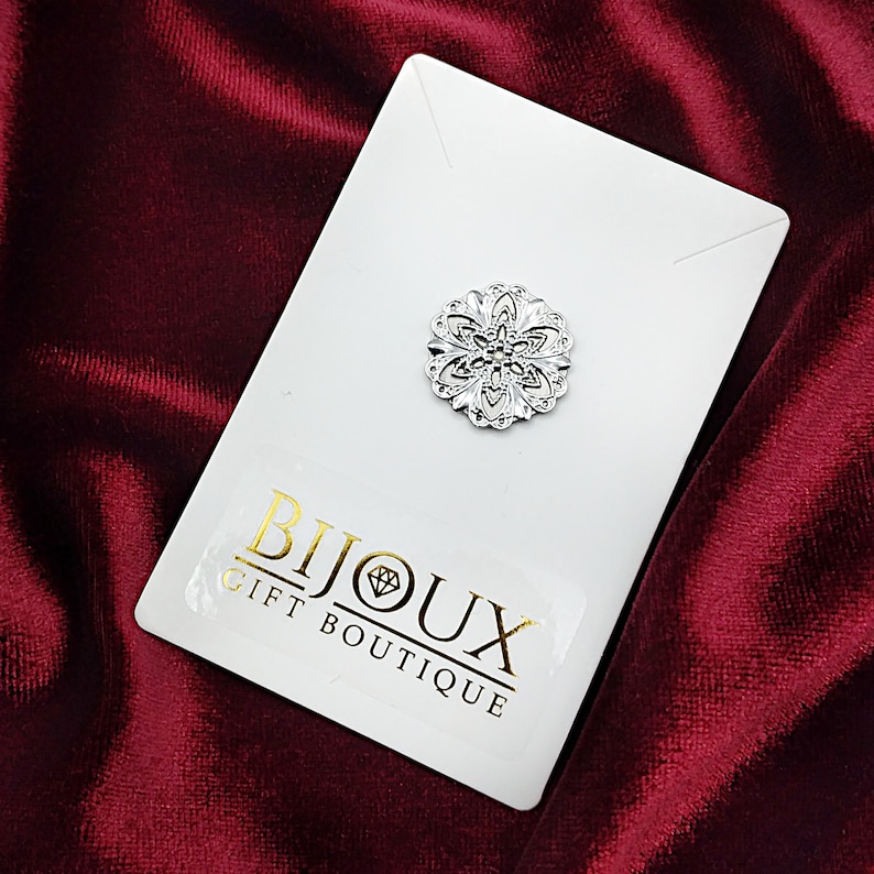 May include: A silver filigree brooch with a floral design. The brooch is on a white card with the text "Bijoux Gift Boutique".