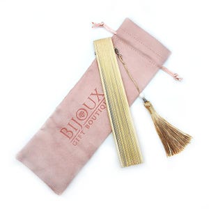 May include: A gold-colored folding fan with a tassel and a pink velvet pouch. The pouch has the text "Bijoux Gift Boutique" printed on it.