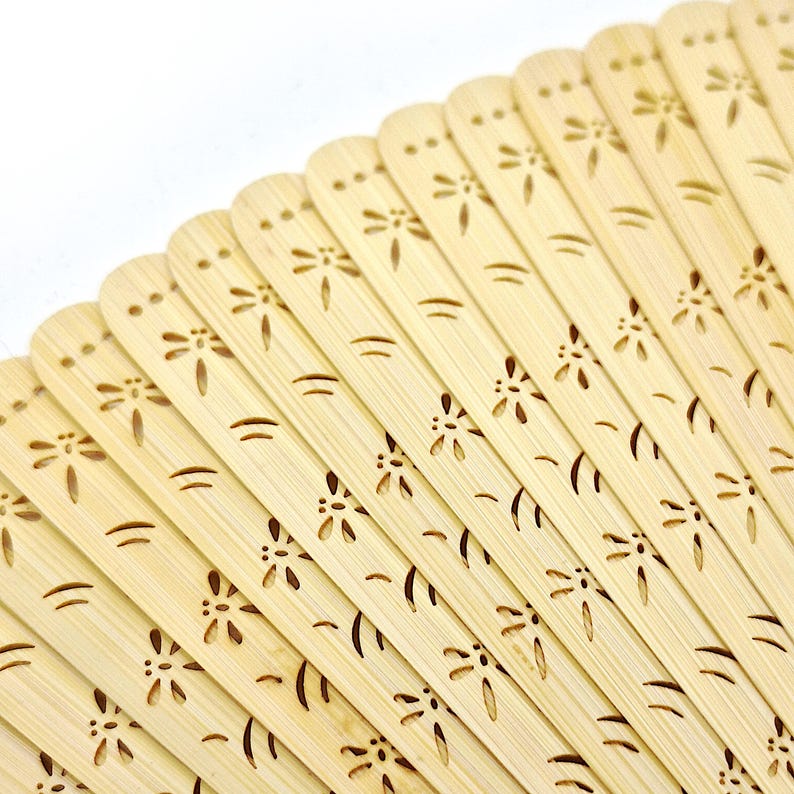 May include: A close-up of a light brown bamboo fan with a floral design. The fan is folded and the intricate details of the carved flowers are visible.