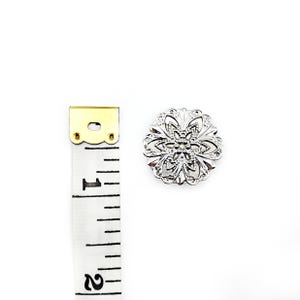 May include: Silver filigree button with a floral design. The button is approximately 1 inch in diameter.