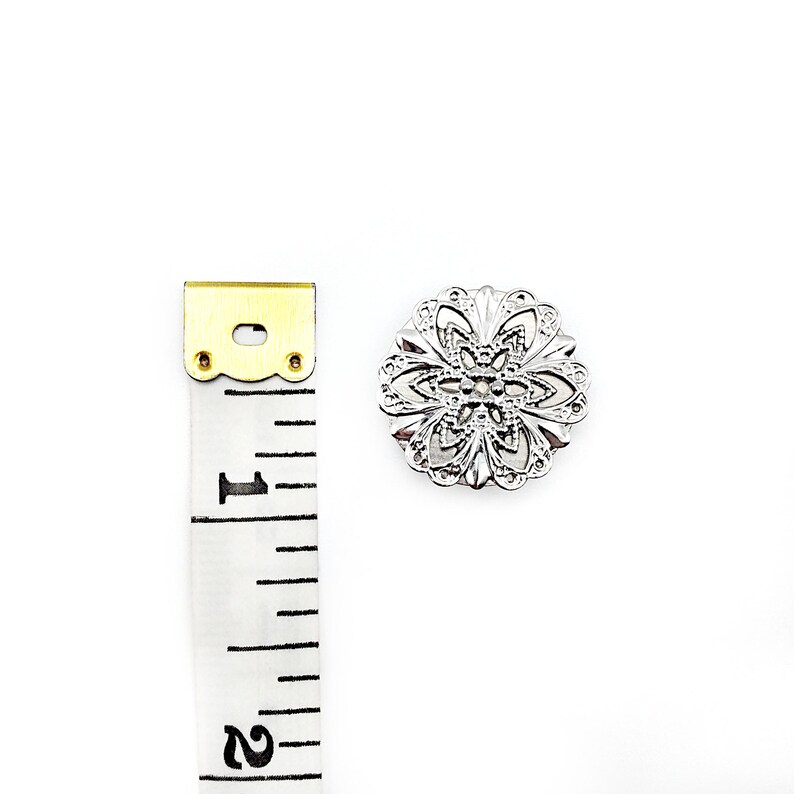 May include: Silver filigree button with a floral design. The button is approximately 1 inch in diameter.
