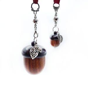May include: Two wooden acorn-shaped charms with silver chains and leaf accents. The larger charm has a dark brown finish and the smaller charm has a lighter brown finish.