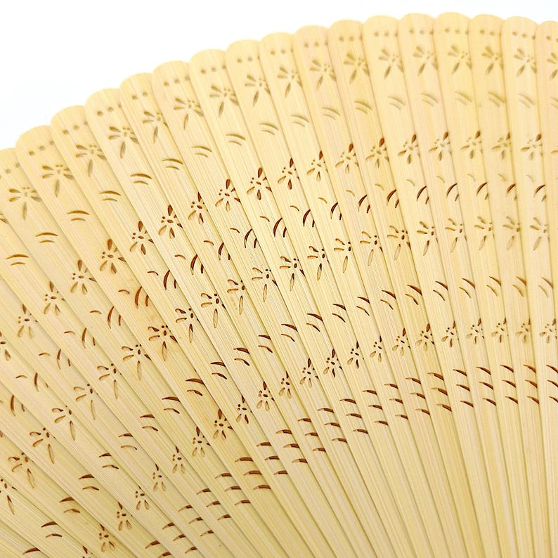 May include: A close-up of a light brown bamboo folding fan with a delicate floral pattern carved into the surface.