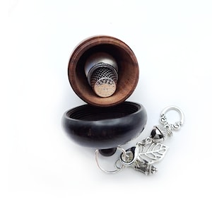 May include: A wooden acorn-shaped trinket box with a silver thimble inside. The box has a silver chain with a charm attached to it. The charm is a silver acorn with a leaf and a small silver thimble.