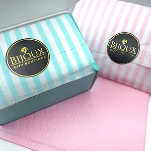 K&ouml;nnte beinhalten: Zwei Geschenkboxen mit einem hellblauen und wei&szlig;en Streifenmuster und einem rosa und wei&szlig;en Streifenmuster. Beide Boxen haben ein schwarzes Kreislogo mit goldener Aufschrift "Bijoux Gift Boutique".
