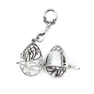 May include: A silver thimble charm with a decorative filigree design. The charm is attached to a silver chain with a lobster clasp.