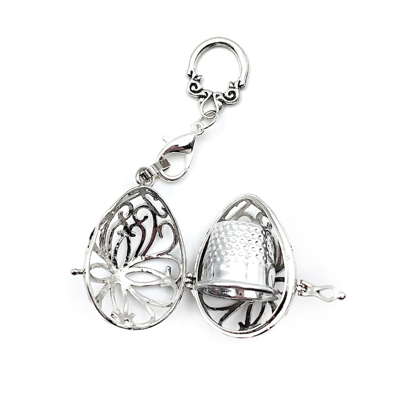 May include: A silver thimble charm with a decorative filigree design. The charm is attached to a silver chain with a lobster clasp.