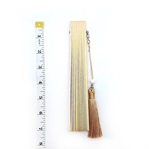 May include: A closed, light brown bamboo folding fan with a tassel and a white bead on a string.