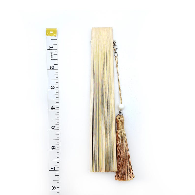 May include: A closed, light brown bamboo folding fan with a tassel and a white bead on a string.