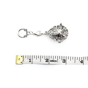 May include: Silver charm with a filigree design and a clasp. The charm is about 1 inch in diameter. A measuring tape is in the background.
