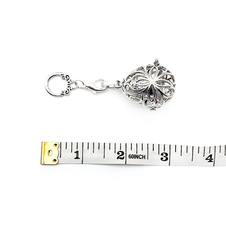 May include: Silver charm with a filigree design and a clasp. The charm is about 1 inch in diameter. A measuring tape is in the background.