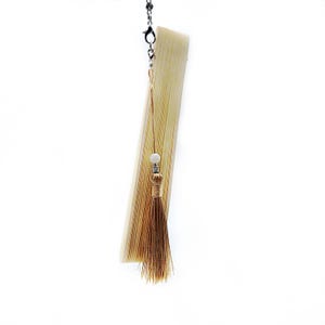 May include: A light brown folding fan with a gold tassel and a white bead. The fan is attached to a silver chain.
