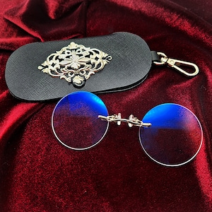 May include: A pair of round, blue-tinted glasses with a silver frame and a black leather case with a silver ornate design.