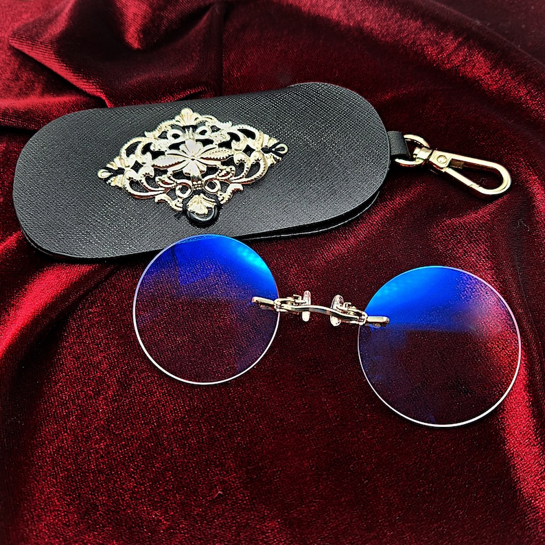 May include: A pair of round, blue-tinted glasses with a silver frame and a black leather case with a silver ornate design.