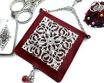 May include: A red velvet sewing kit with a silver filigree design and a chain. The kit has a small red bead tassel and a silver clasp.