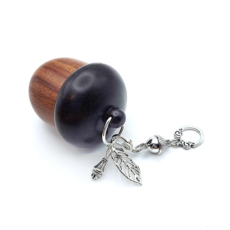 May include: A wooden acorn-shaped box with a silver chain and charms, including a leaf and an acorn. The box is made of dark wood and has a light brown top.
