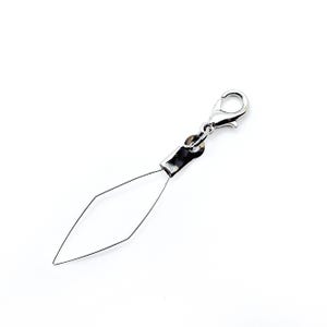 Pode incluir: Um passador de agulha prateado com um fecho de lagosta. O passador apresenta um la&ccedil;o de arame em forma de diamante preso a uma manga e fecho de metal, projetado para facilitar a passagem da agulha. O fundo &eacute; branco liso.