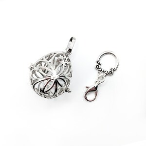 May include: A silver charm with a delicate, intricate design. The charm is shaped like a teardrop and has a small loop at the top for attaching to a necklace or bracelet. The charm is made of metal and has a shiny finish.