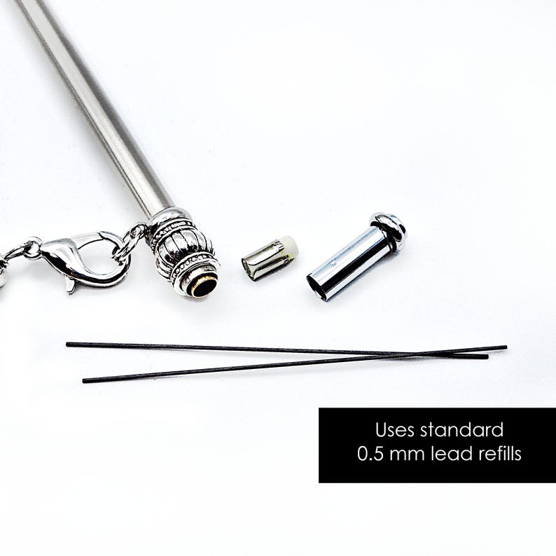 May include: A silver mechanical pencil with a decorative ribbed end, a lobster clasp attachment, a small eraser, a metal cap, and two thin black leads. The text on the image states: Uses standard 0.5 mm lead refills.