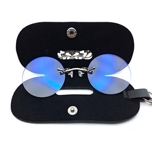 May include: A pair of blue tinted round glasses with a silver frame and a black leather case. The case has a silver clasp and a silver decorative piece on the front.