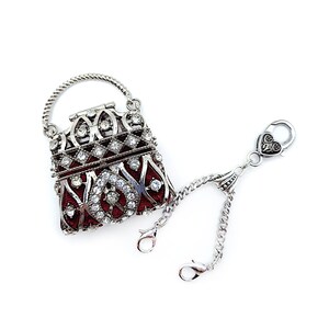 K&ouml;nnte beinhalten: Ein kleiner, verzierter, rot-silberner Handtaschenanh&auml;nger mit einem gedrehten Griff und einer Kette mit zwei Verschl&uuml;ssen. Die Tasche ist mit klaren Strasssteinen besetzt und hat ein detailliertes Vintage-Design.