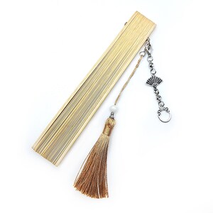 May include: A wooden folding fan with a brown tassel and a silver charm. The charm is a decorative fan shape with a chain attached.