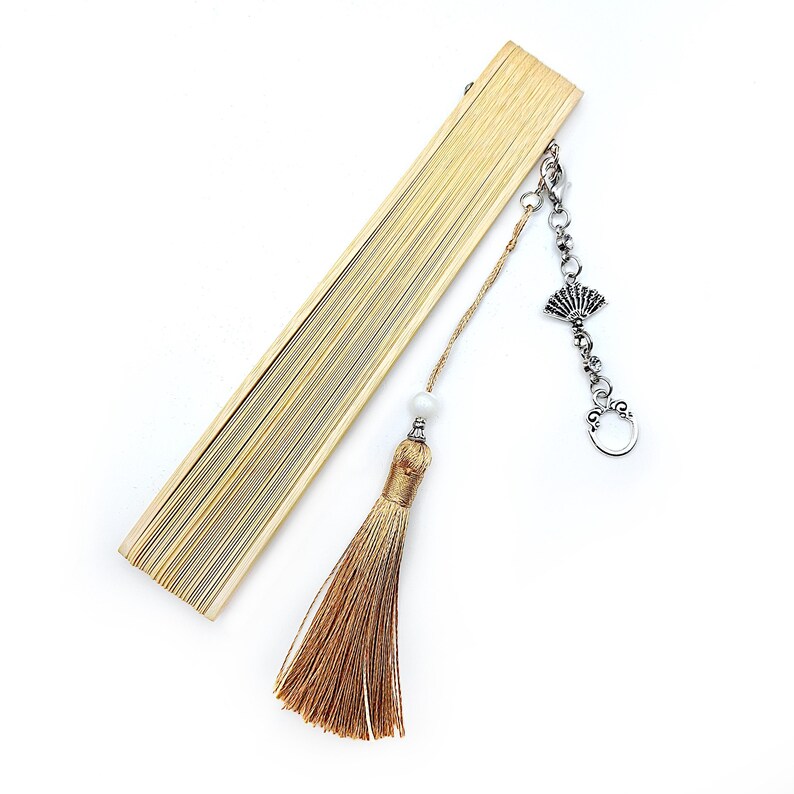 May include: A wooden folding fan with a brown tassel and a silver charm. The charm is a decorative fan shape with a chain attached.