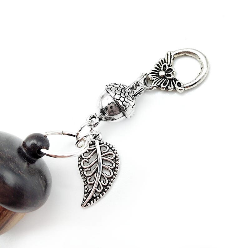 May include: A silver acorn charm with a silver leaf charm and a silver butterfly charm attached to a silver ring. The charms are attached to a wooden acorn.