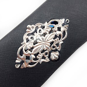 May include: A silver filigree hair clip with a floral design. The clip is on a black background.