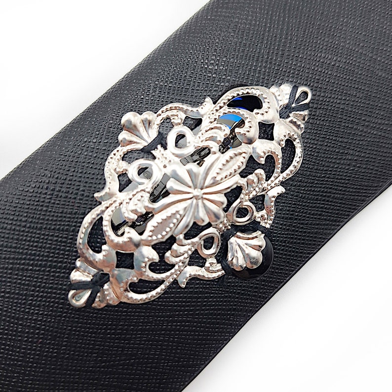 May include: A silver filigree hair clip with a floral design. The clip is on a black background.