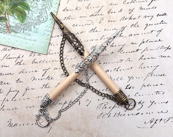 May include: Two wooden knitting needles connected by a metal chain. One needle features a dark bronze-toned filigree cap, while the other has a silver-toned filigree cap. Both needles have matching metal end caps and a small circular ring attached.