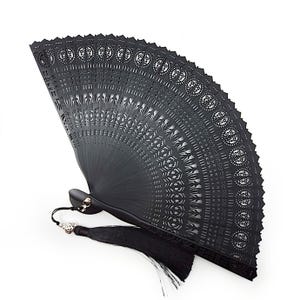 May include: A black, intricately carved folding fan with a tassel. The fan features a detailed openwork design with circular and geometric patterns. The handle is black, and the tassel is attached with a silver-colored bead.
