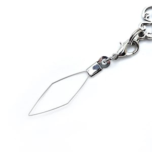 Pode incluir: Um berloque de joia prateado com um design de arame em forma de diamante. O berloque &eacute; preso a um fecho lagosta e a uma corrente decorativa. O fundo &eacute; branco.