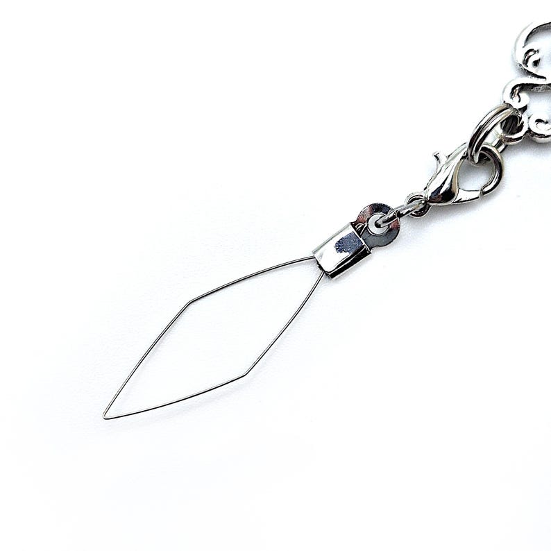 Pode incluir: Um berloque de joia prateado com um design de arame em forma de diamante. O berloque &eacute; preso a um fecho lagosta e a uma corrente decorativa. O fundo &eacute; branco.