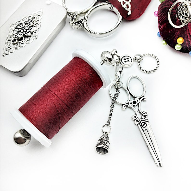May include: A silver sewing kit charm with a red spool of thread, a pair of scissors, a thimble, and a button.