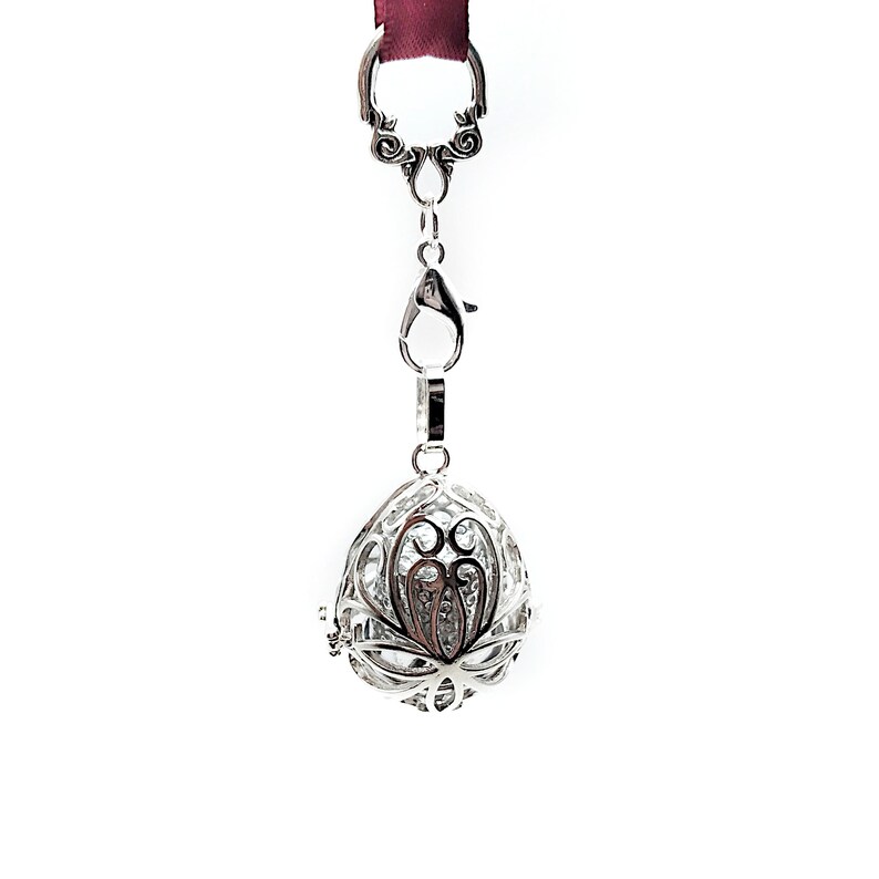 May include: Silver charm with a delicate, intricate design. The charm is shaped like an egg and has a floral pattern. It hangs from a silver chain with a lobster clasp.