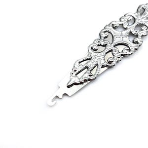 May include: A silver metal hook tool with a decorative, ornate design. The tool has a small loop at one end and a pointed end at the other.