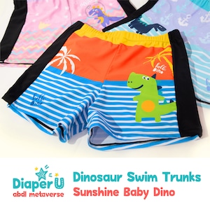 Op de afbeelding: Oranje, blauwe en groene zwembroek met een dinosaurusprint en de tekst "Hello Dino". De zwembroek heeft zwarte zijpanelen en een wit gestreept patroon.