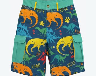 Può includere: Pantaloncini cargo blu con motivo a dinosauri. I pantaloncini presentano dinosauri arancioni, gialli, verdi e blu, con la scritta "ROAR" stampata sopra. I pantaloncini hanno due tasche turchese e una cintura turchese.