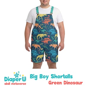 May include: Green dinosaur print shortalls with teal straps. The shortalls feature a dark teal background with colorful dinosaur illustrations in yellow, orange, and blue. The text "Big Boy Shortalls Green Dinosaur" is visible.