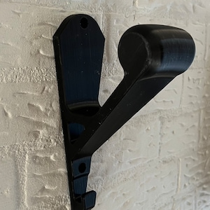 Peut inclure: Crochet noir en plastique à fixer au mur, avec un sommet arrondi et un crochet en bas. Le crochet est conçu pour tenir une variété d'articles, tels que des manteaux, des chapeaux ou des sacs.