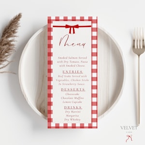 May include: A red and white checkered menu card with a bow design at the top, listing menu items such as Smoked Salmon, Beef Stake, Cheesecake, and Dry Martini. The menu is placed on a white plate with a fork and knife.