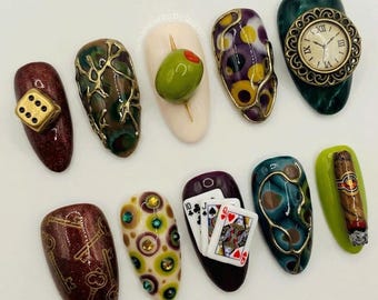 May include: A set of ten press-on nails featuring diverse 3D designs including a gold die, a green olive, a vintage clock face, playing cards, keys, and a cigar. Each nail showcases unique textures, metallic accents, and vibrant colors.
