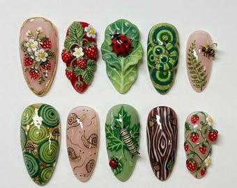 Könnte beinhalten: Ein Set aus zehn künstlichen Fingernägeln mit detaillierten Naturmotiven, darunter Erdbeeren, ein Marienkäfer auf einem Blatt, eine Biene, Schnecken, eine Raupe, Eicheln und Holzmaserungsmuster. Jeder Nagel zeigt eine einzigartige Illustration.