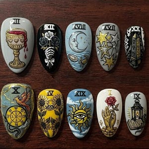 May include: A set of ten almond-shaped press-on nails featuring detailed hand-painted tarot card designs. Each nail displays unique imagery including a golden chalice, roses, a crescent moon, stars, sunflowers, a sun with an eye, and a lantern.