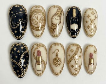 Könnte beinhalten: Ein Set aus zehn mandelförmigen Press-on-Nägeln mit Luxusmotiven. Die Designs zeigen schwarze und cremefarbene Hintergründe mit goldenen Prägedetails wie Handtasche, Uhr, Armbanduhr, Champagnerflasche, Lippenstift, Rosenohrring und Monogramm-Logos.
