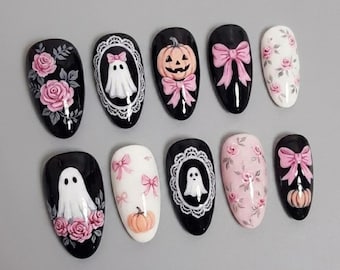 May include: A set of ten press-on nails featuring a variety of designs including pink roses on black and light pink backgrounds, white ghosts framed in lace, orange jack-o'-lanterns with pink bows, and light pink bows on black and white bases.