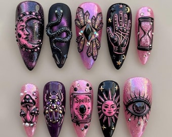 Könnte beinhalten: Ein Set aus zehn künstlichen Fingernägeln in einer dunklen und rosa Farbpalette mit mystischen Motiven wie einer Mondsichel, einer Schlange, Kristallen, einer Handlesehand, einer Sanduhr, Pilzen, einem Käfer, einem Zauberbuch, einer Sonne und einem Auge.