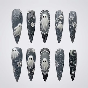 May include: A set of ten stiletto-shaped press-on nails in a dark gray base color. The designs feature raised white 3D relief art including ghosts, floral vines, and small pearl-like accents. Some nails are framed with a border of tiny white beads.